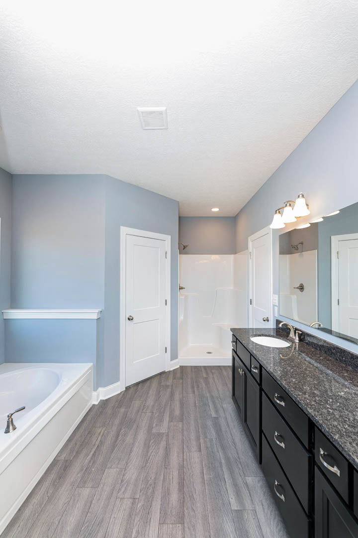 Bathroom with freestanding white bathtub, wood flooring, white vanity with silver faucet, and white door with silver knobs