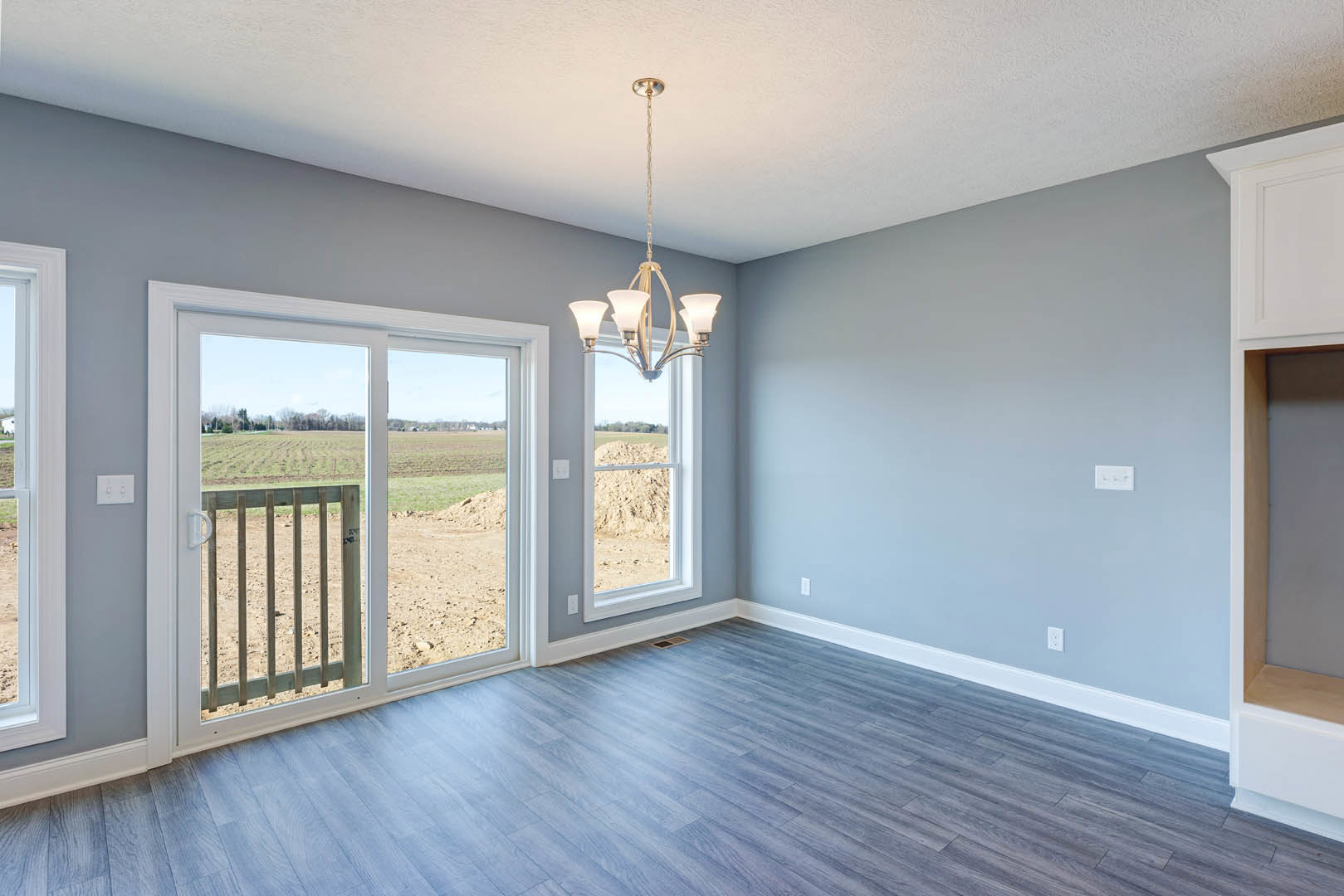 Hardwood floor room with white walls, sliding glass door opening to fenced field, modern chandelier hanging from ceiling