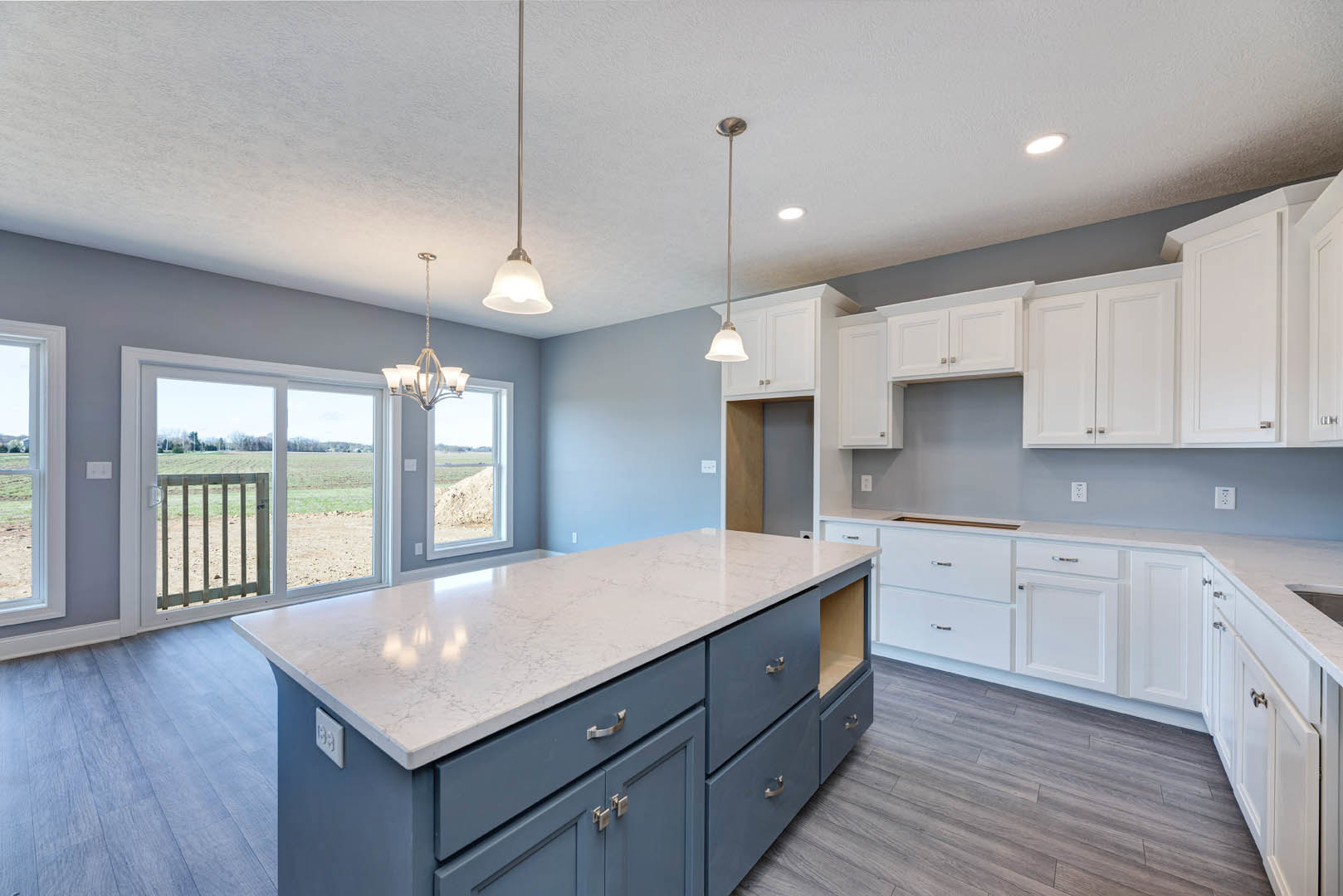 Spacious kitchen featuring a large white island with built-in sink, light cabinetry, stainless steel appliances, and wide windows overlooking a grassy yard.