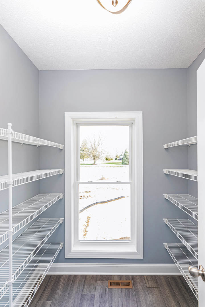 Built-in white shelves along a plaster wall, large window overlooking snowy yard, wood floor with floor vent