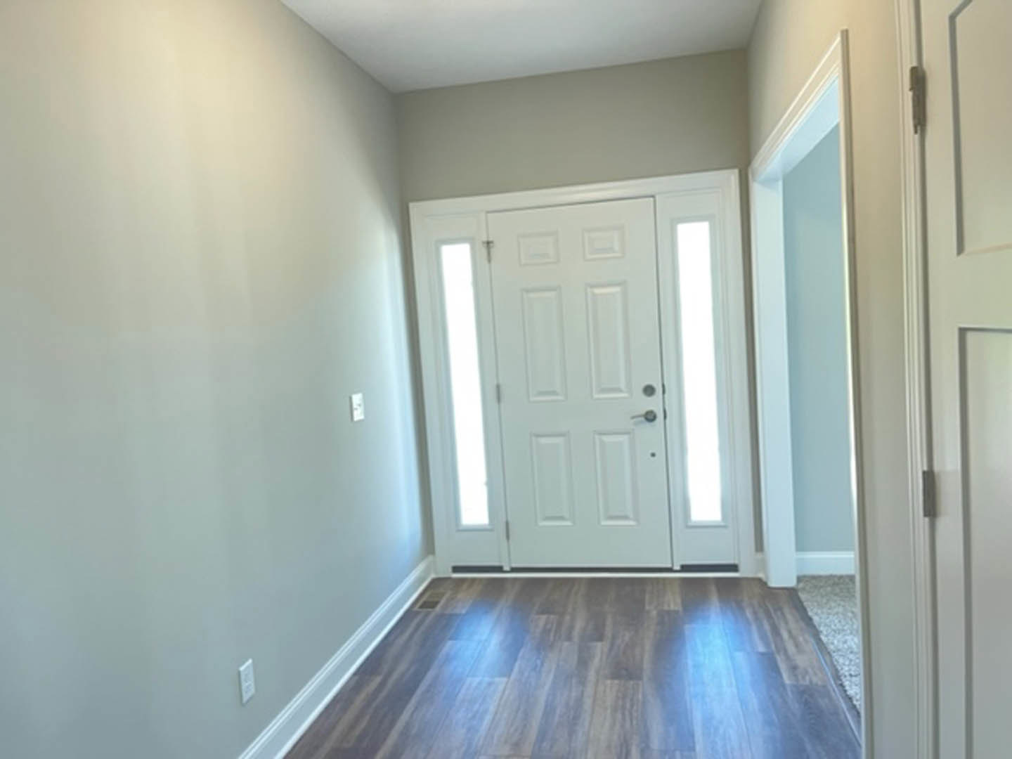 Hallway with light wood flooring, white walls, white ceiling, and a white door featuring a glass panel and black accent stripe