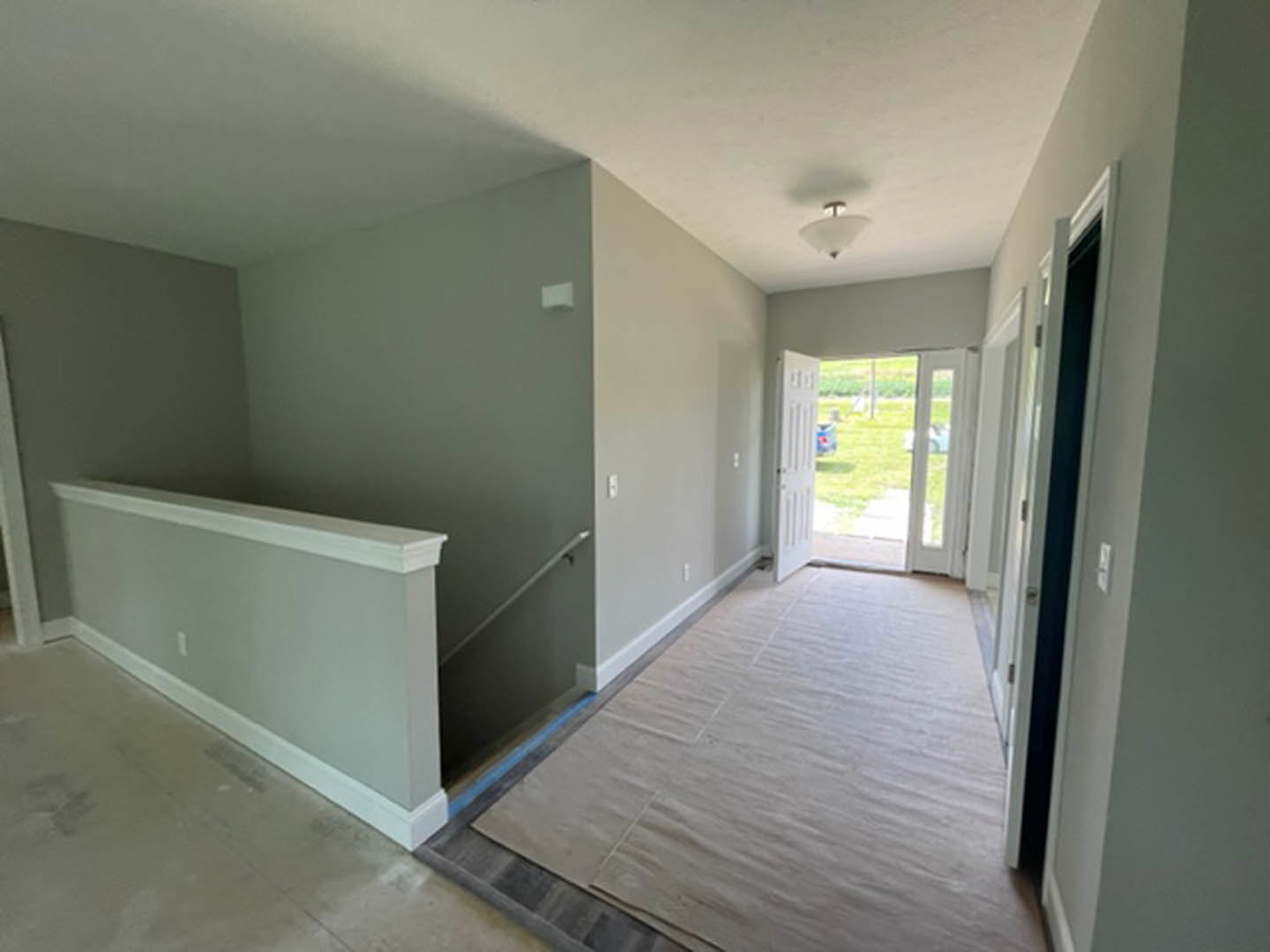 Hallway with carpeted floor, white trim walls, staircase with wooden railing, ceiling light fixture, open white door leading to yard