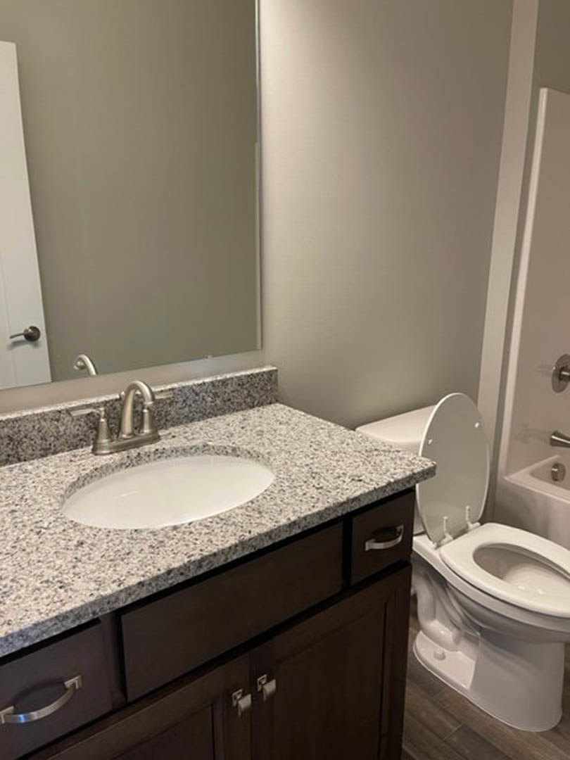 Modern bathroom with white porcelain sink, chrome faucet, and matching toilet set against light gray tile walls and quartz countertop
