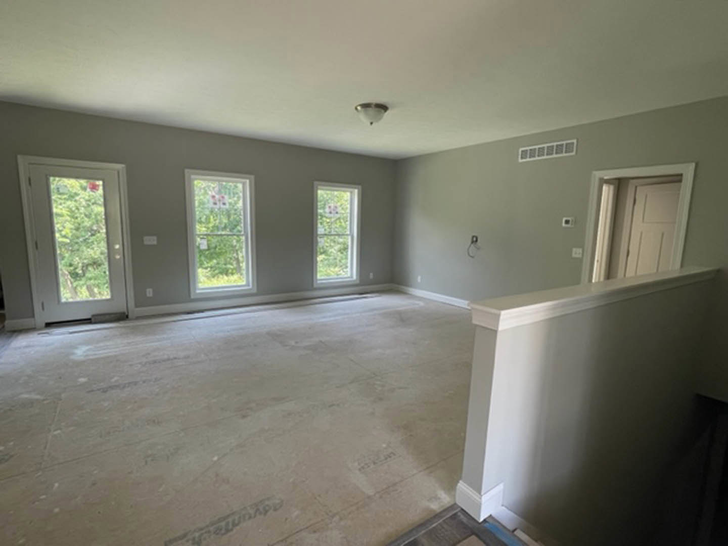 Open living area featuring a white staircase with matching railing, multiple large windows, a ceiling vent, recessed lighting, and a white door with glass inset.