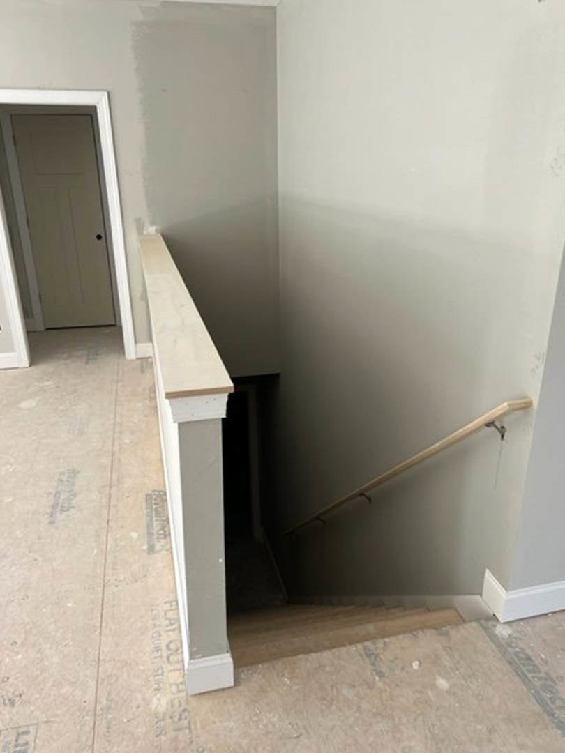 White staircase with wooden handrail ascending beside a white wall with crown molding, black accent wall, and white door featuring a black knob