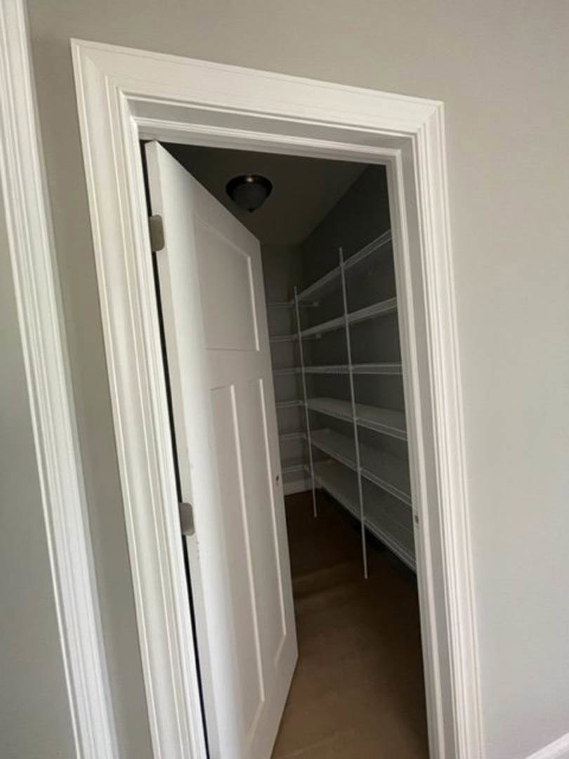 White paneled door with chrome handle opens to a closet featuring built-in white shelves against plaster walls and light wood flooring