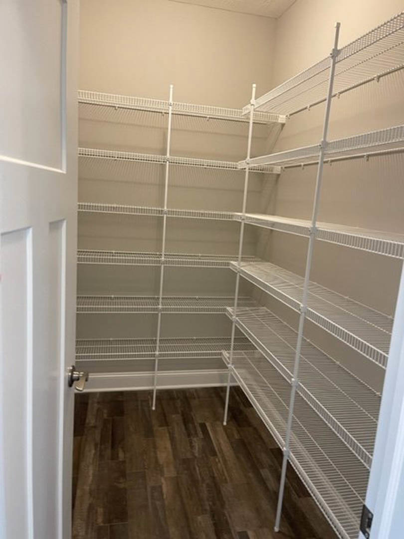 Walk-in closet featuring white built-in shelves, wood plank flooring, and a white door with plaster walls