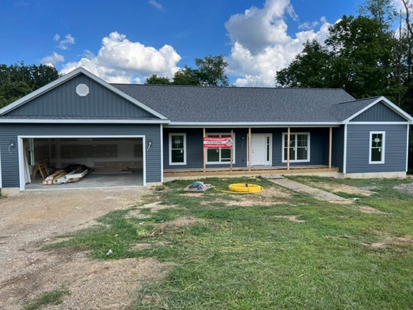 Two-story house with attached garage, white siding, front porch, manicured lawn, and leafy trees under a partly cloudy sky