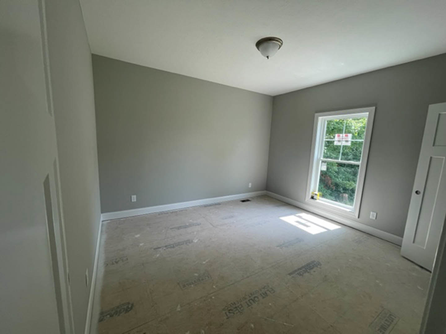 Bright room with plaster walls, large window, white tile flooring, wooden door, and modern light fixture.