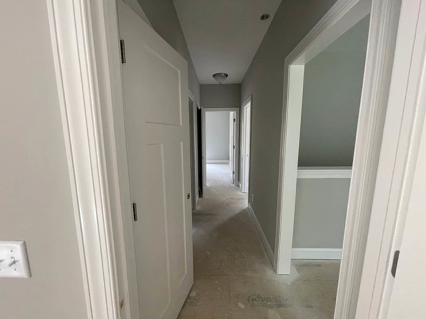 Hallway with white paneled doors, tile flooring, plaster walls, and a modern ceiling light fixture