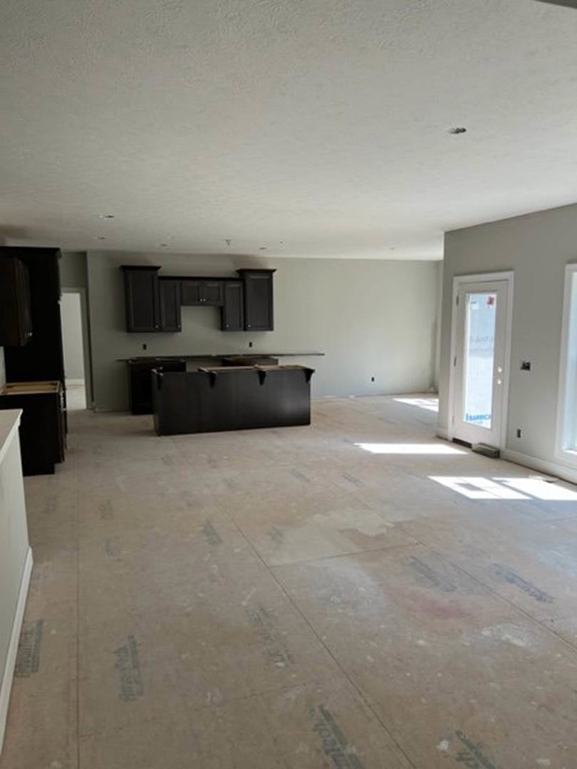 Modern kitchen with black upper cabinets, white walls, black rectangular range hood with metal bar, white tile flooring, large window, and sleek door adjacent to a built-in desk