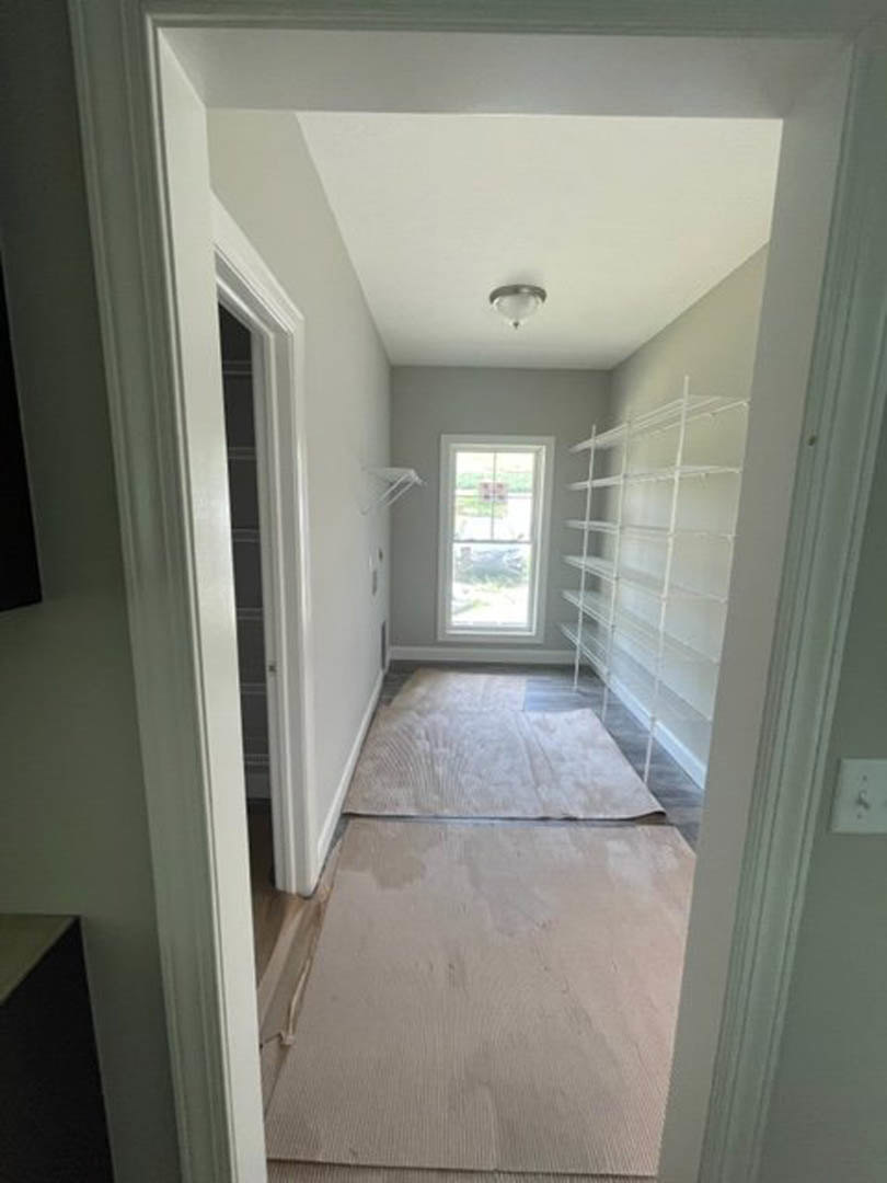 Hallway with built-in white shelves, large window with exterior sign visible, white carpet flooring, ceiling light fixture, plaster walls with molding