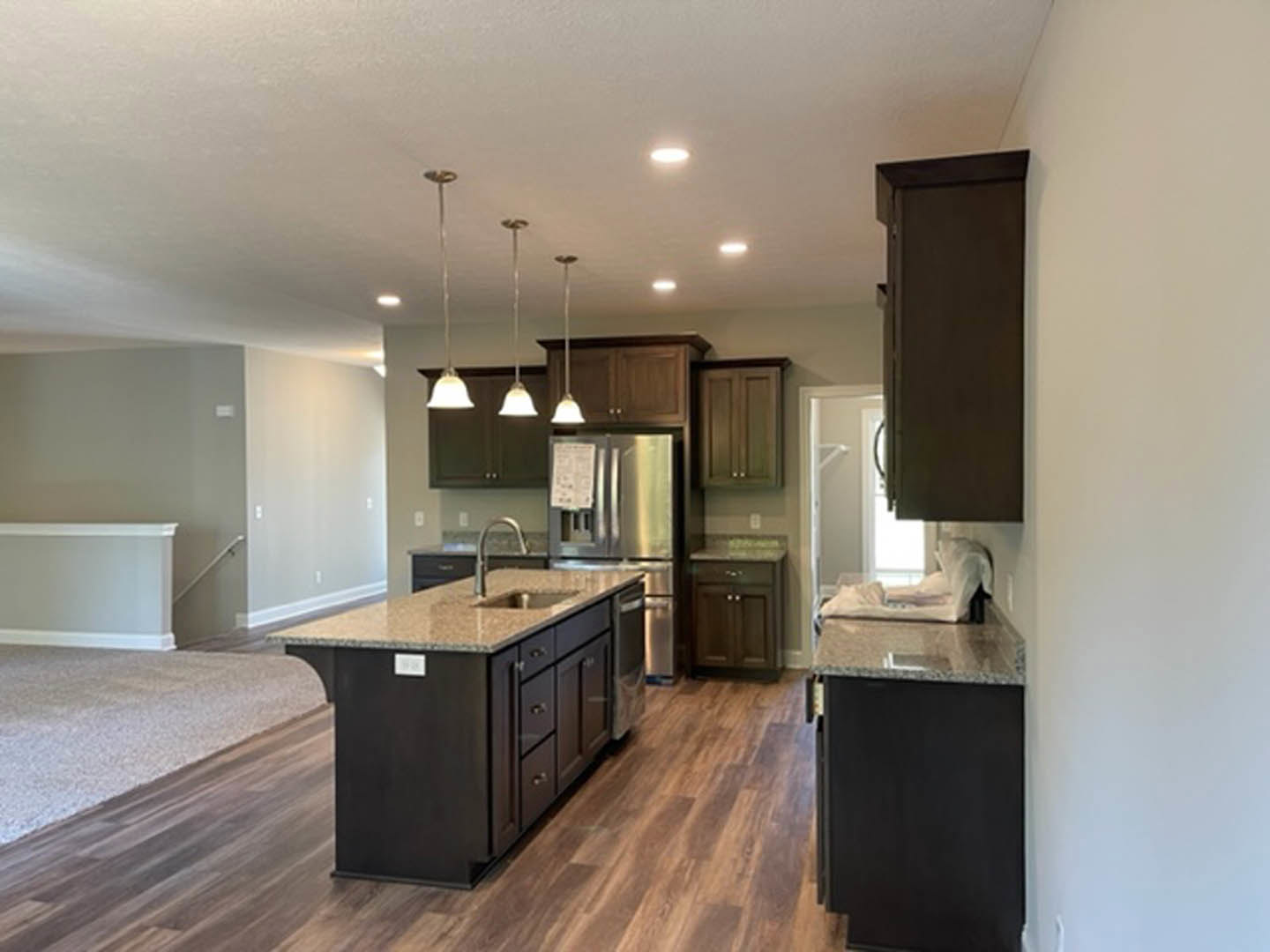 Kitchen with hardwood flooring, wood cabinetry, central island featuring a sink, stainless steel refrigerator, and light-colored countertops