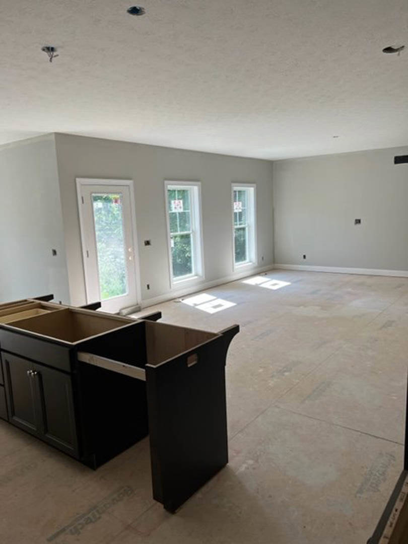 Modern kitchen featuring a central island with open drawers, black cabinetry, wood flooring, a dining table, white-framed window, and a white door with glass panel.