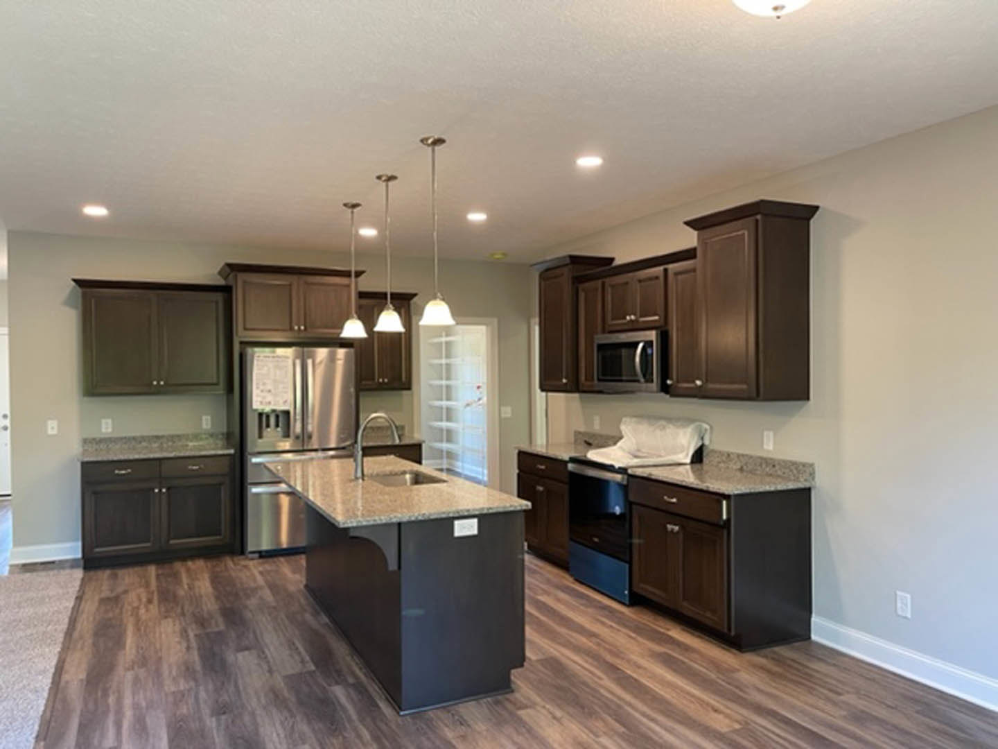 Kitchen with dark wood cabinets, stainless steel refrigerator, granite island countertop, built-in microwave, dishwasher, and light-colored flooring
