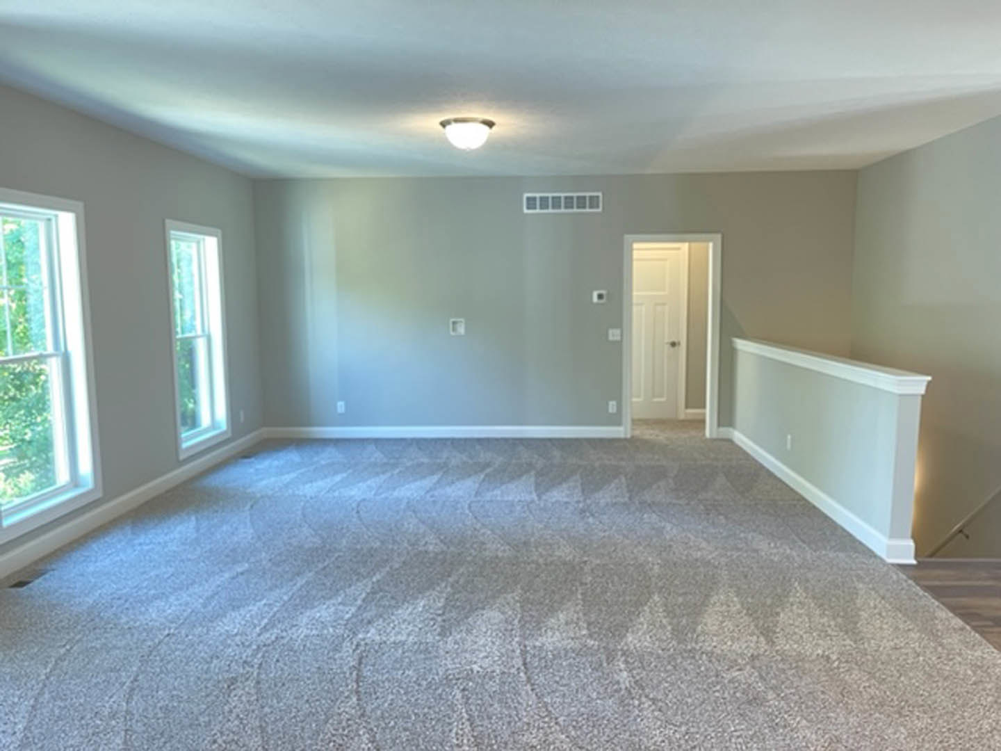 Carpeted room with white walls, white door, white railing, window with white frame, ceiling light fixture, and plaster molding.