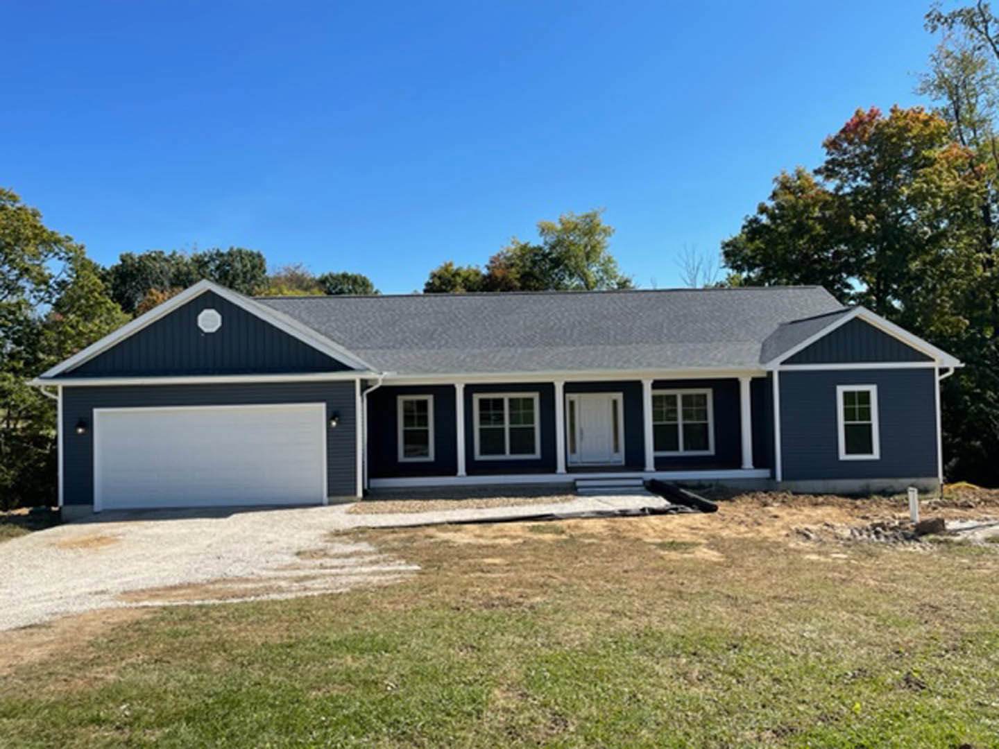 Blue siding house with white columns, glass-paneled front door, attached garage, white-framed windows, and grassy front yard