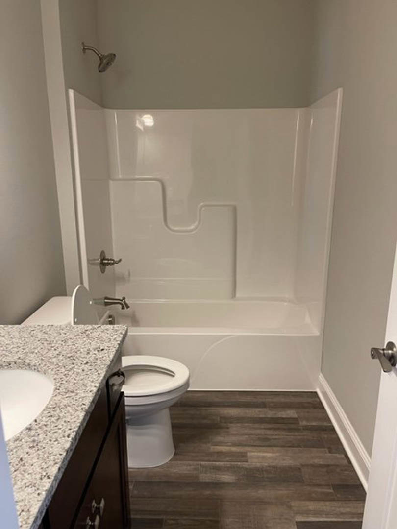 Bathroom with white toilet and sink, curved white bathtub, wood flooring, light tile walls, chrome fixtures