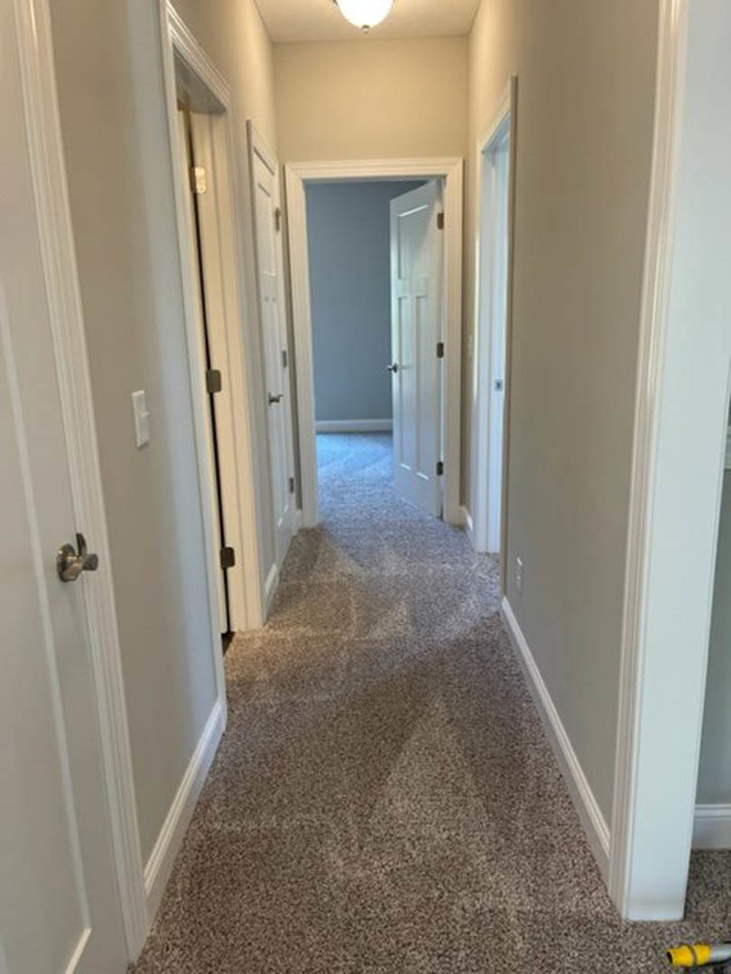 Hallway with white walls, carpeted floor, and multiple white doors; close-up of a silver door knob; blue accent wall visible near one door