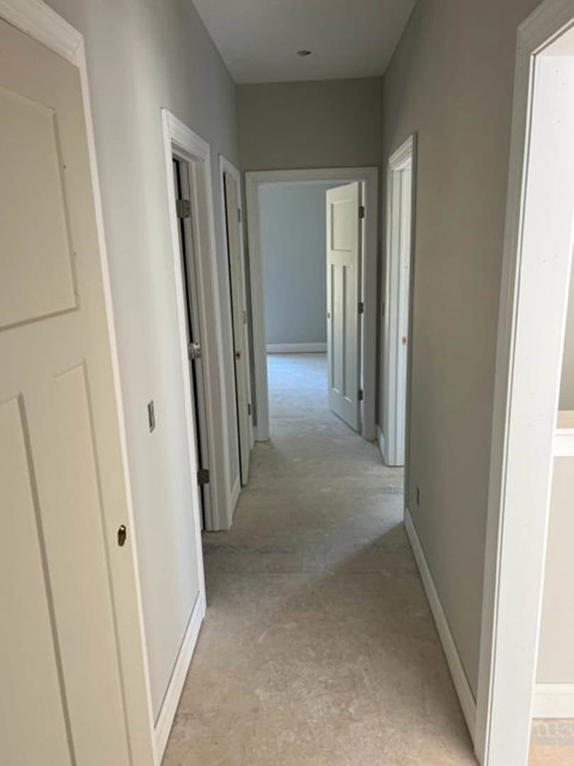 Hallway with white plaster walls, multiple white doors, light-colored flooring, and simple door frames