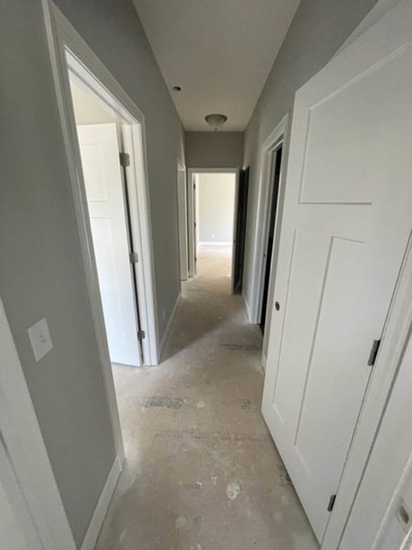 Hallway with smooth white walls, multiple white panel doors, silver door handles, and light-colored flooring