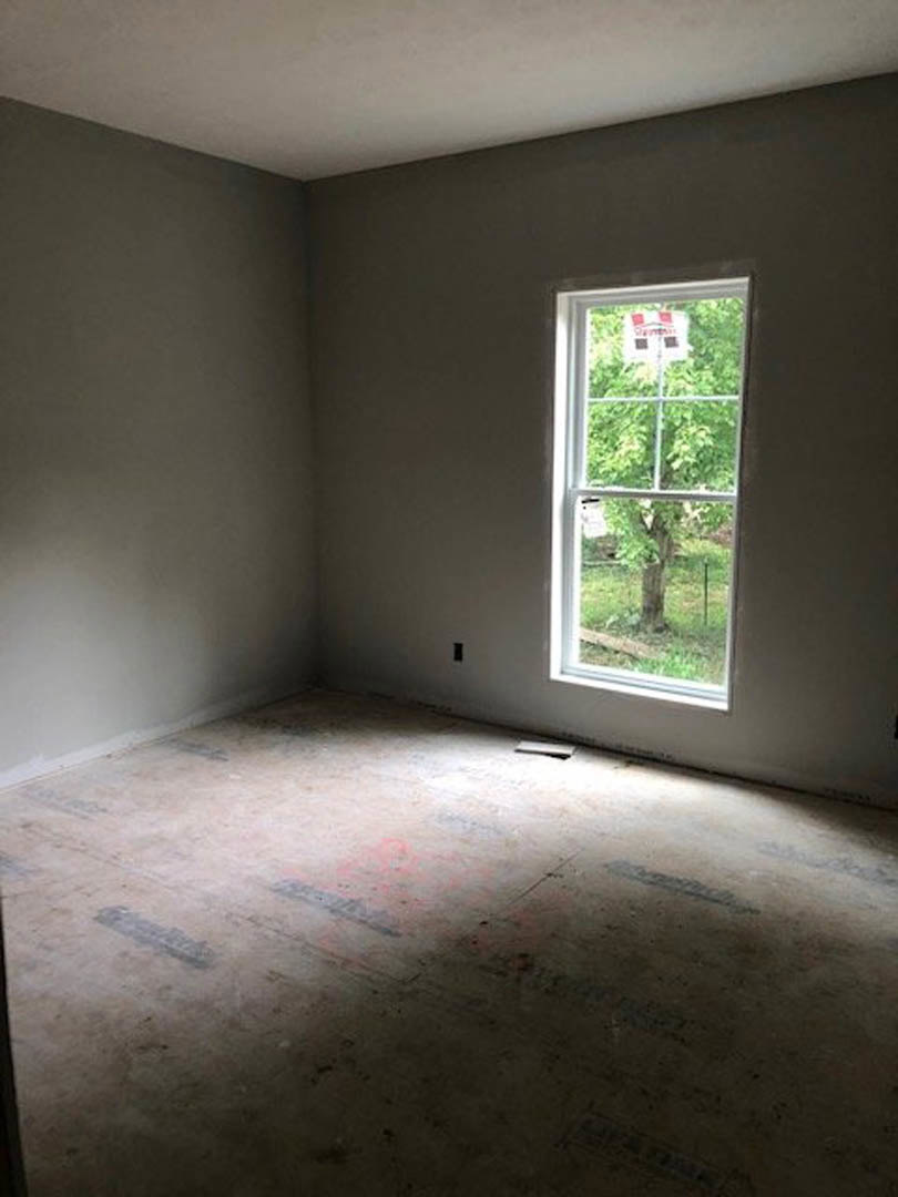 White plaster walls with black trim, large window framing view of leafy tree, light wood flooring, natural daylight filling modern room