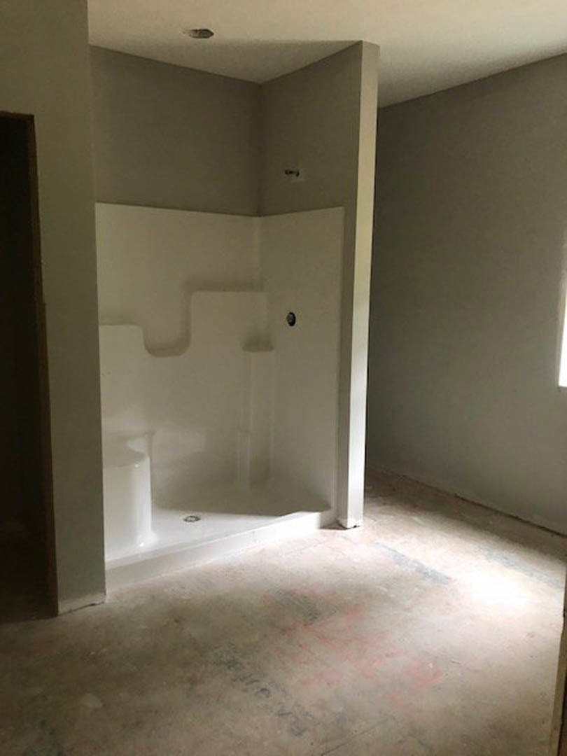 Bathroom with walk-in shower, white bathtub, grey tile flooring, plaster walls, large window, and dark wooden door