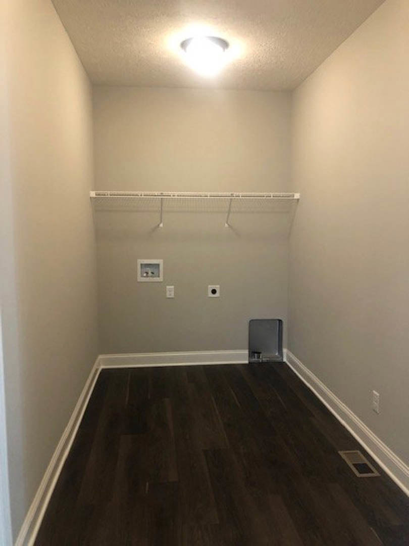 Walk-in closet with dark wood flooring, white plaster walls, ceiling light fixture, and a metal-framed glass door