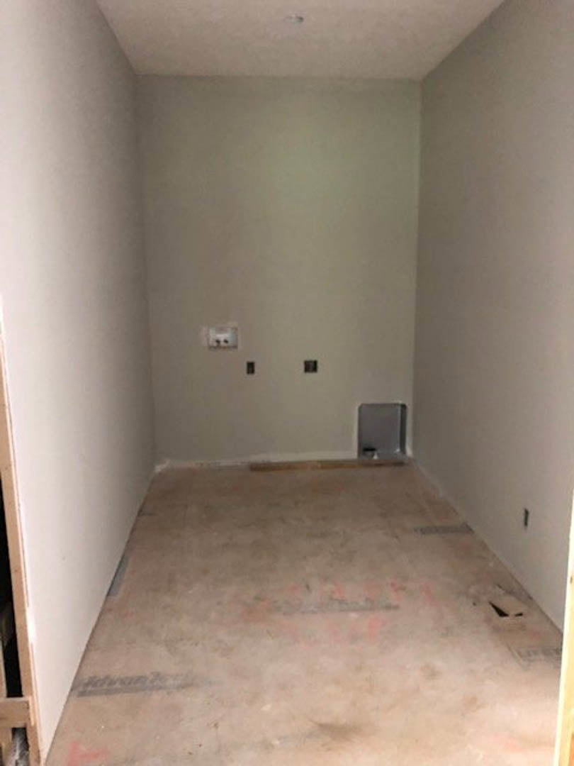 White plaster wall and ceiling, light wood flooring, open door leading to adjacent room, visible light switch and electrical box.