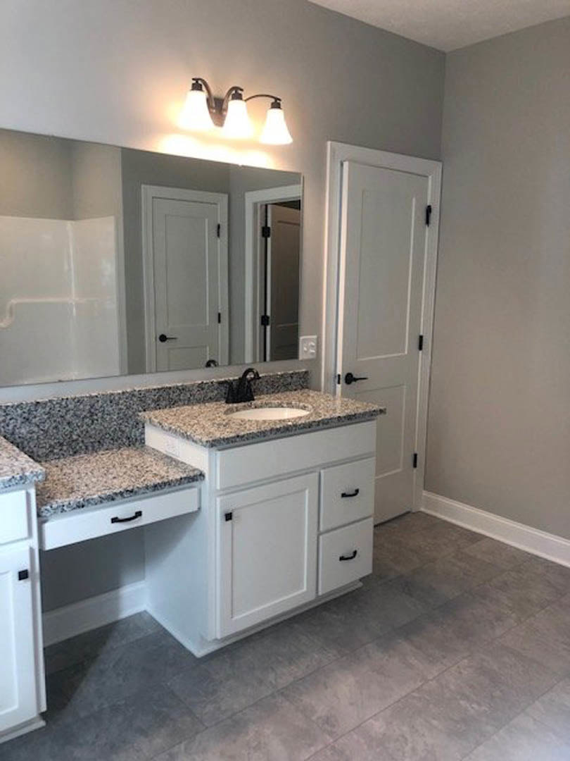 Marble bathroom countertop with white cabinetry, integrated sink, black hardware, close-up of modern light fixture, and black bag resting on stone surface