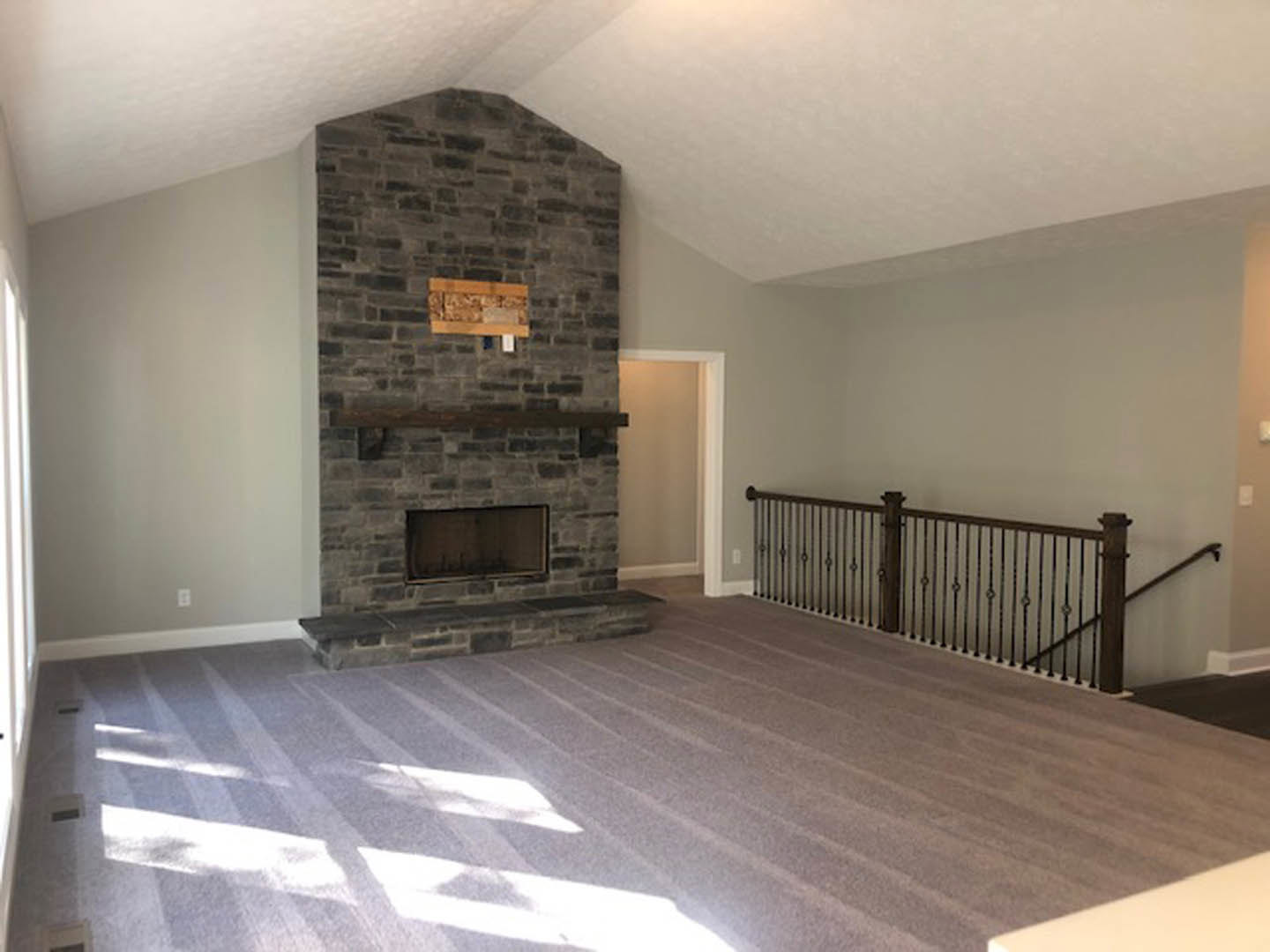 Carpeted living room featuring a brick fireplace with wood mantel, white walls, staircase with wood railing, and wall-mounted light fixture.