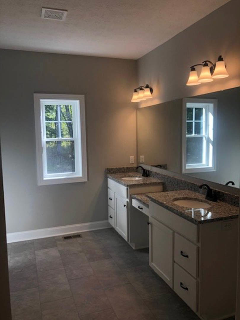 Bathroom with double sinks set in a light stone countertop, large framed mirror above, white cabinetry below, tile flooring, ceiling vent, modern multi-bulb light fixture, and