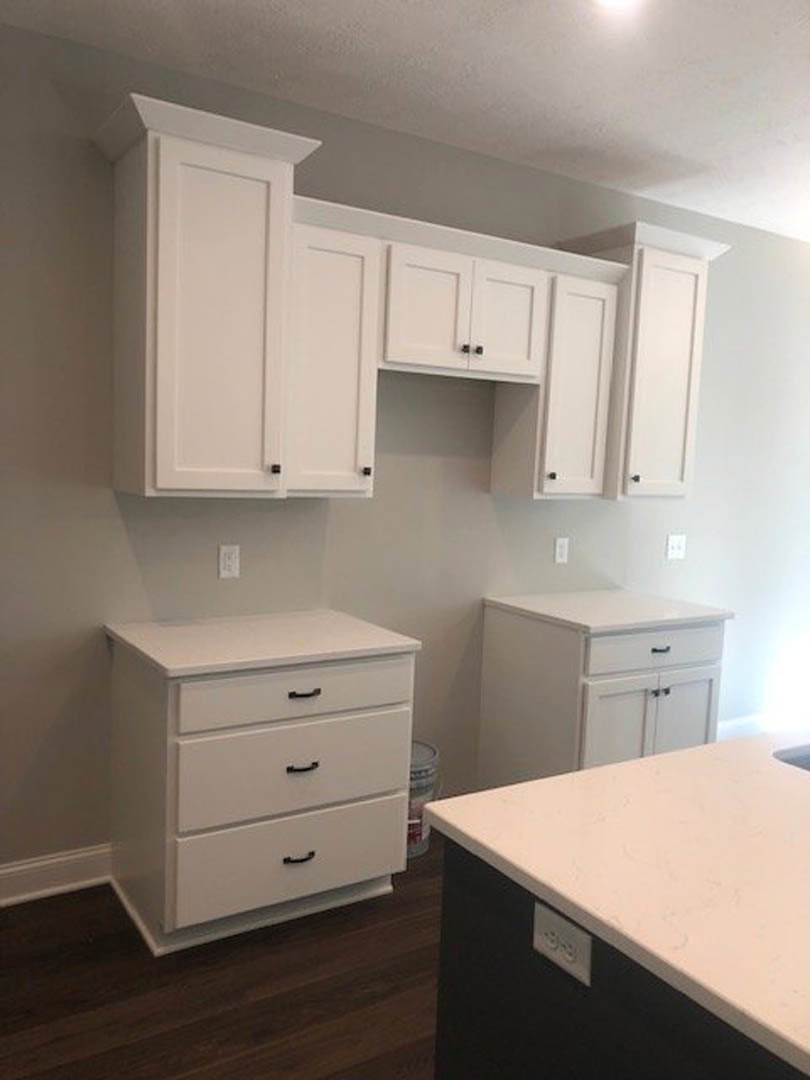 White kitchen with shaker-style cabinets, black hardware, white quartz countertop, and integrated drawers.