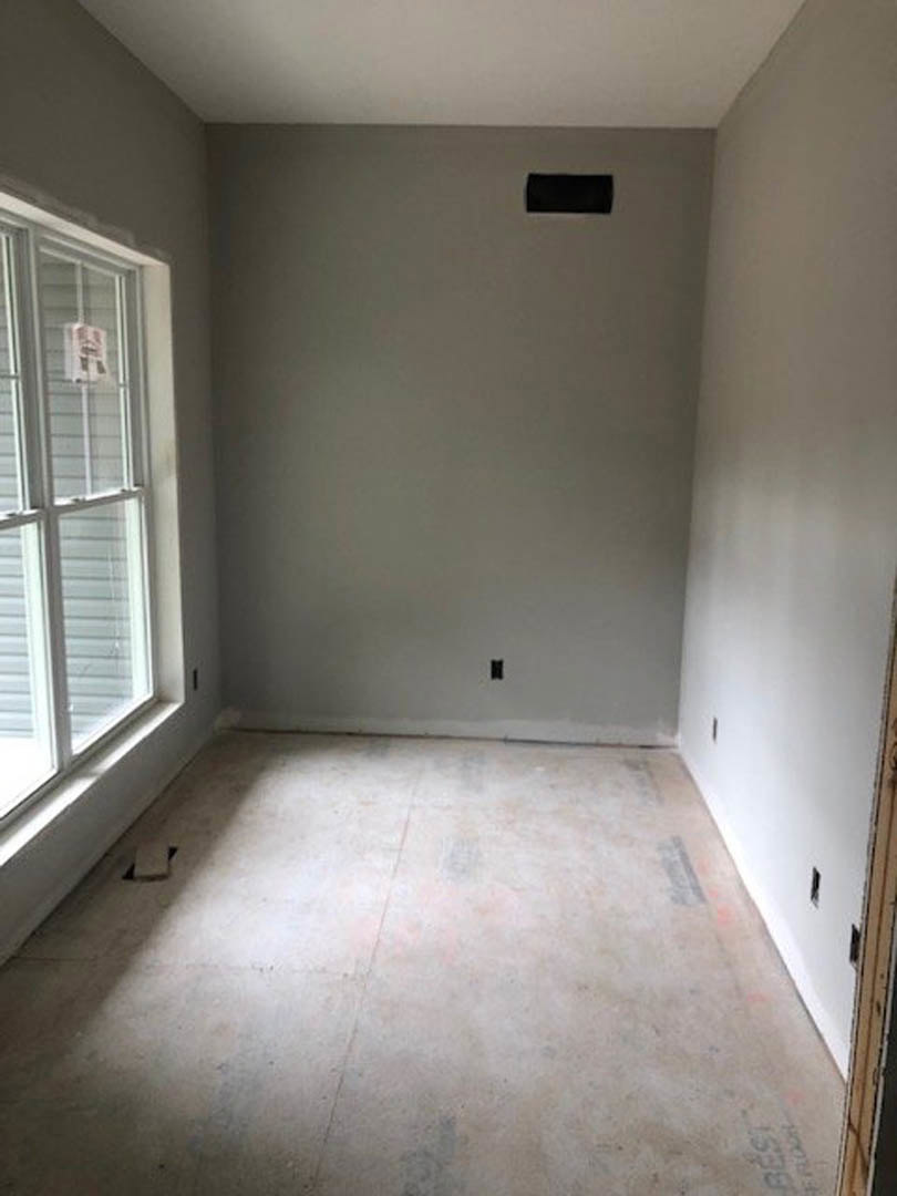 Sunlit room with white plaster walls, large window framed in black, and light laminate flooring.