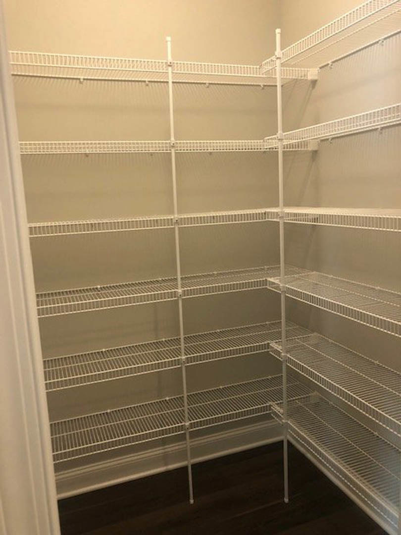 Empty closet with white metal rod and white shelves above dark wood flooring