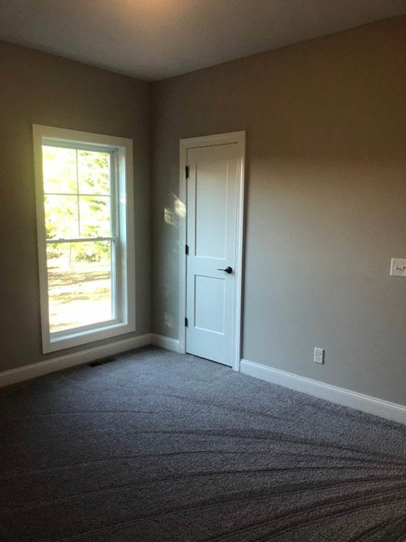 White door with black handle and white-framed window overlooking blue sky, grey carpet flooring, white walls
