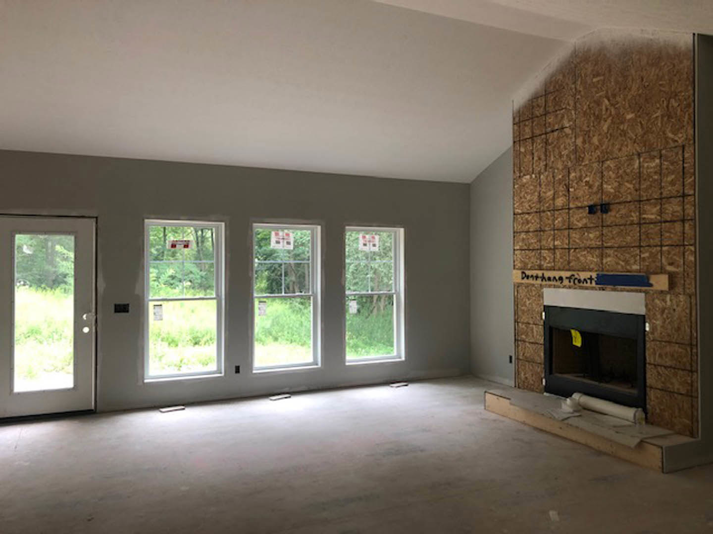Living room with white-framed windows, glass-paneled door, wood flooring, built-in wood shelf, and fireplace with yellow paper on the mantel.