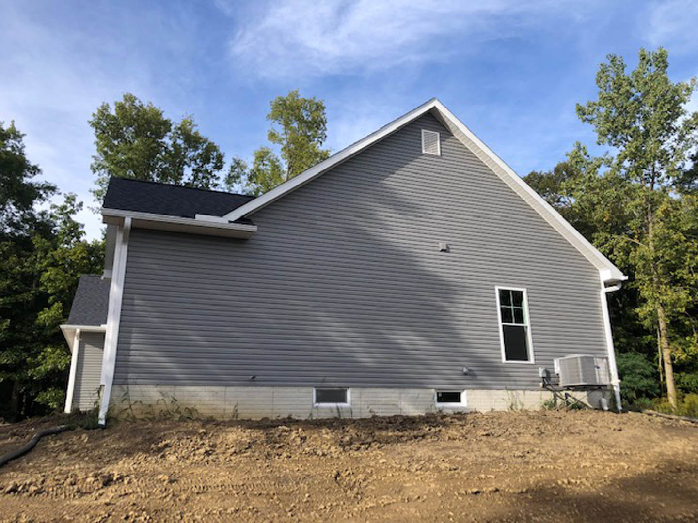 Modern cottage-style home with white roof and siding, surrounded by dirt landscaping and mature trees, large windows with white frames, partly cloudy sky overhead.