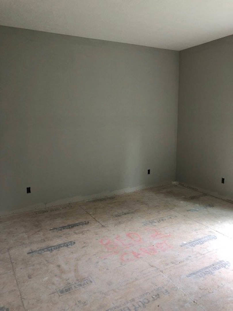 Room with grey and white plaster walls, black flooring, and red writing visible on the floor