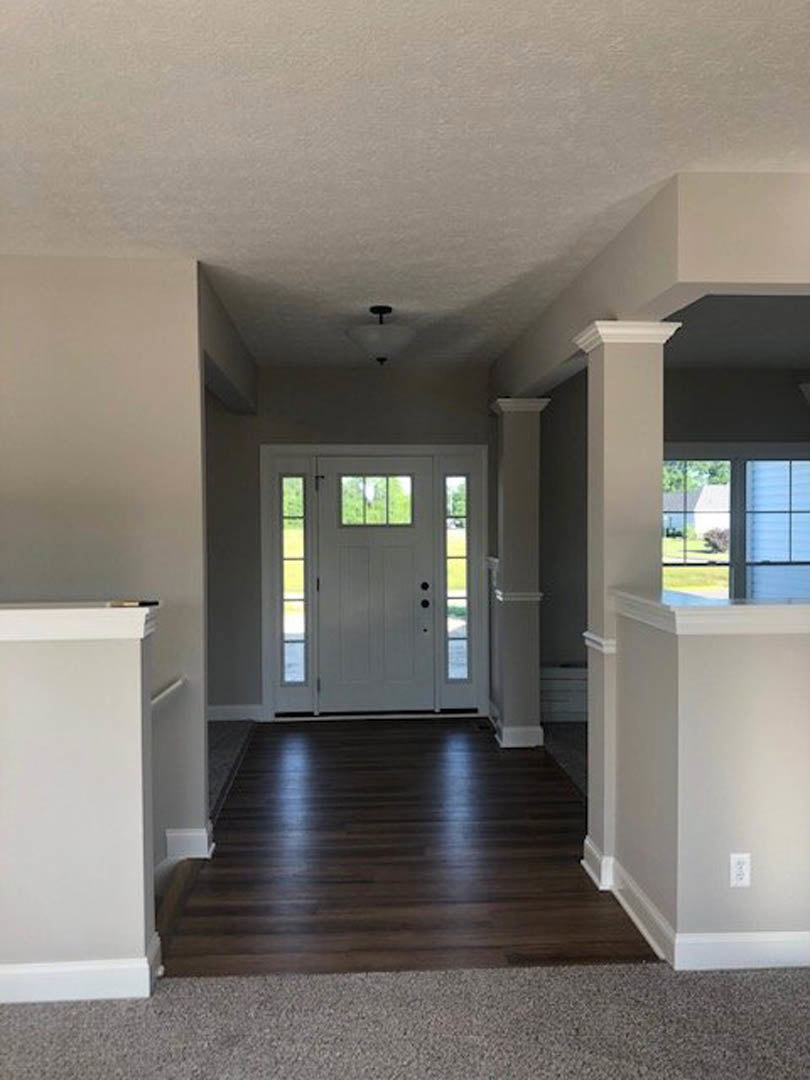 Hallway with dark wood flooring, white walls with grey trim, white door featuring glass panes, ceiling light fixture, window showing blue sky