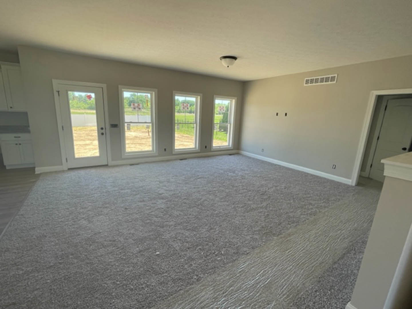 Carpeted room featuring multiple windows, white walls, ceiling vent, and a door with visible light fixture