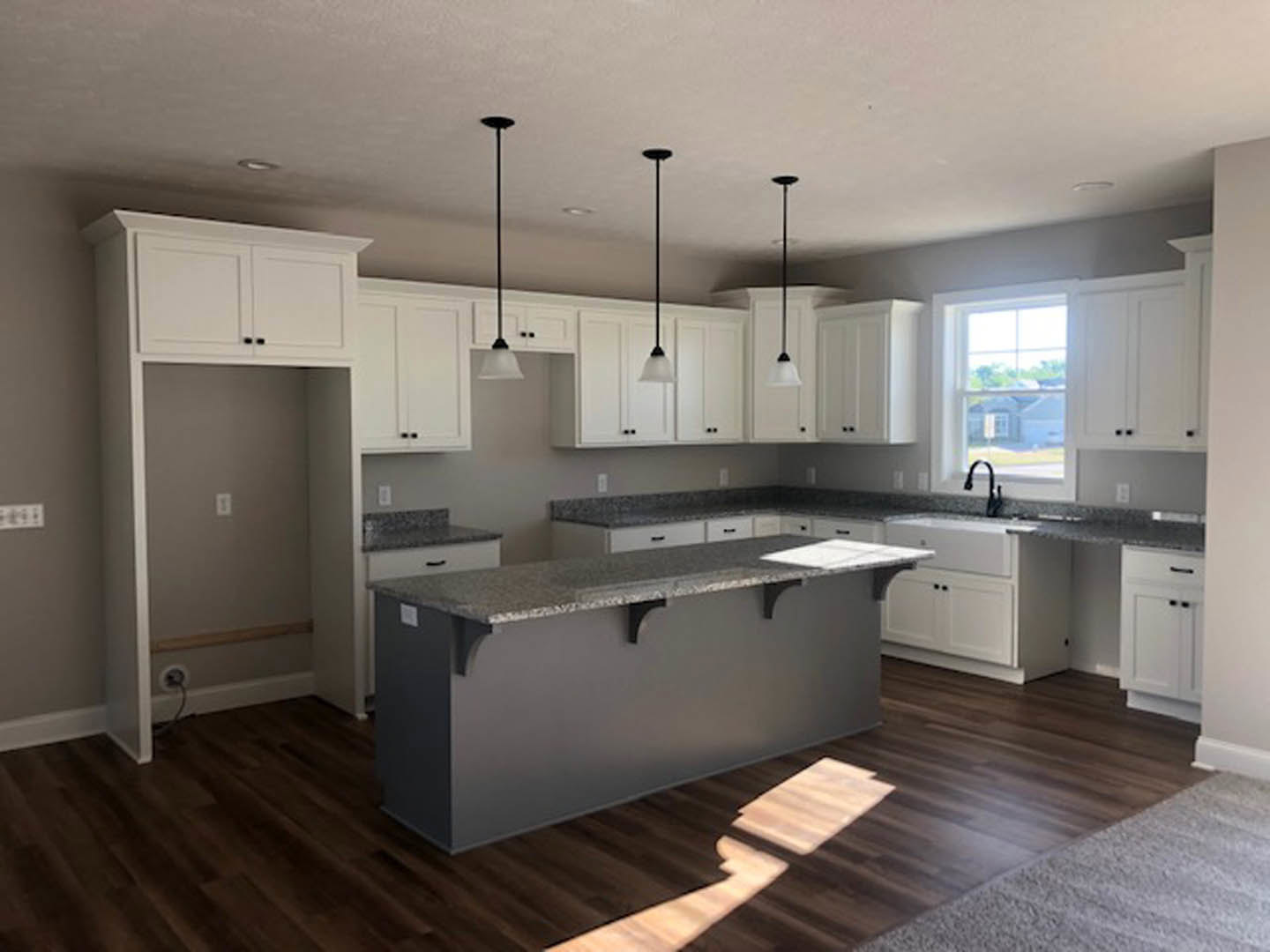 Spacious kitchen featuring a large central island with stone countertop, white cabinetry, tile backsplash, stainless steel sink, pendant lighting, and wide windows overlooking