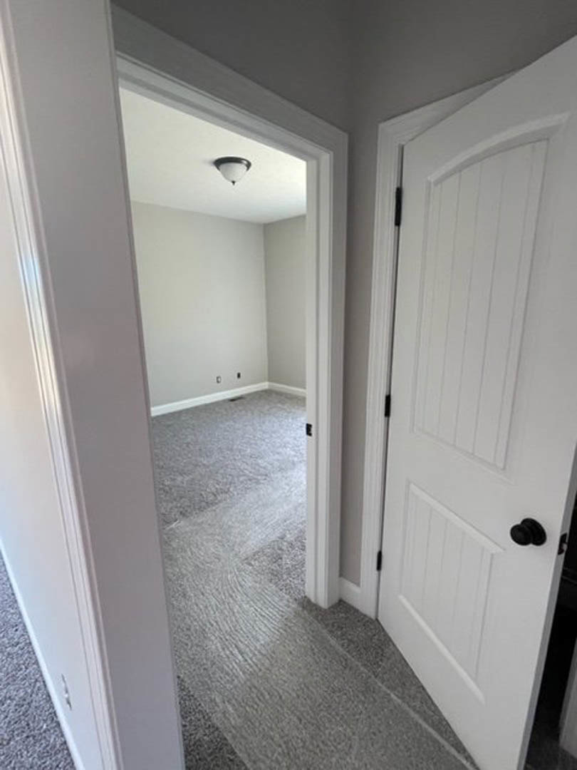 White paneled door with chrome handle in a carpeted hallway, light grey walls, recessed ceiling fixture, and white baseboards