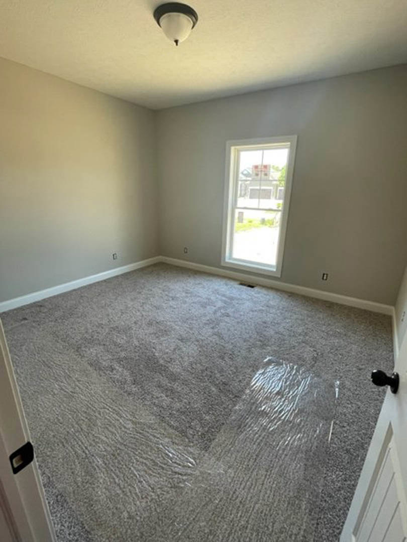 Carpeted room with white plaster walls, large window overlooking street, recessed ceiling light, and grey carpet flooring