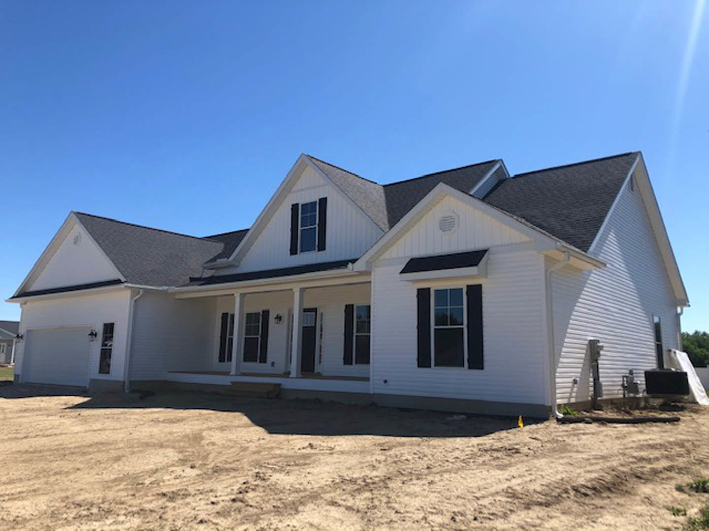 White house with black shutters, white framed windows with multiple panes, vent on white siding, dirt yard in front