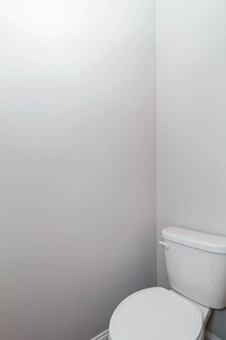 White porcelain toilet with closed lid, set against light-colored bathroom wall and tiled floor.