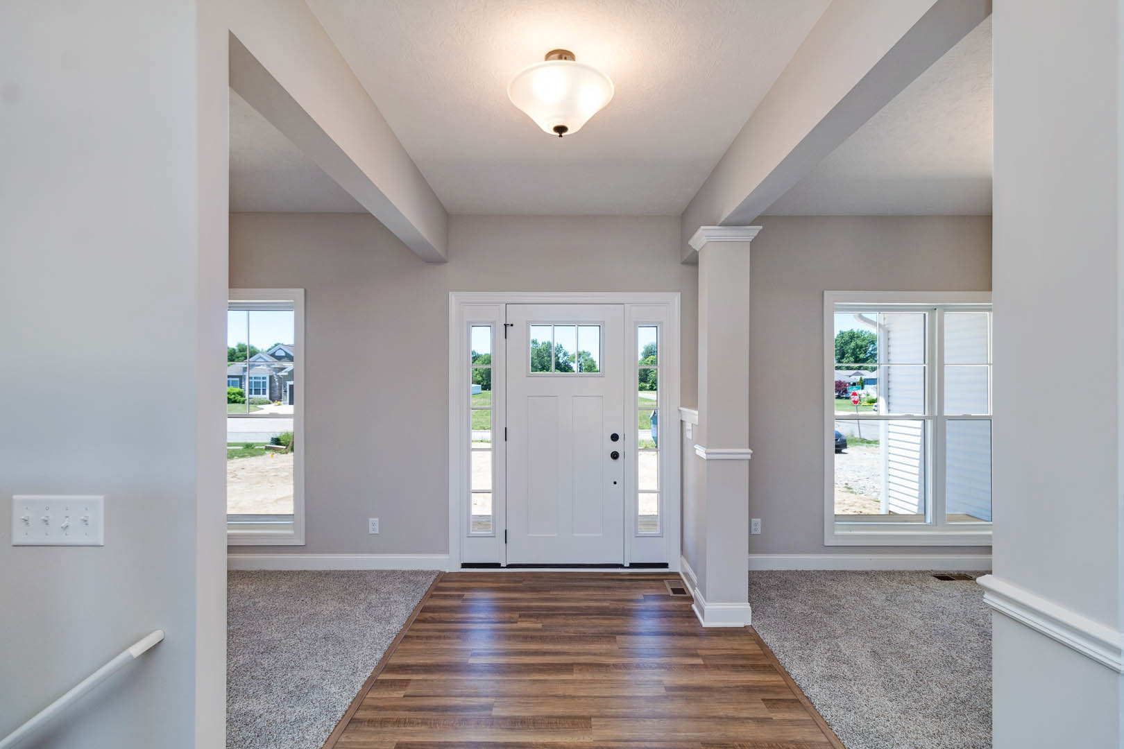 Hallway with white paneled door featuring glass inserts, hardwood flooring, wall-mounted heater, ceiling light fixture, and window overlooking street
