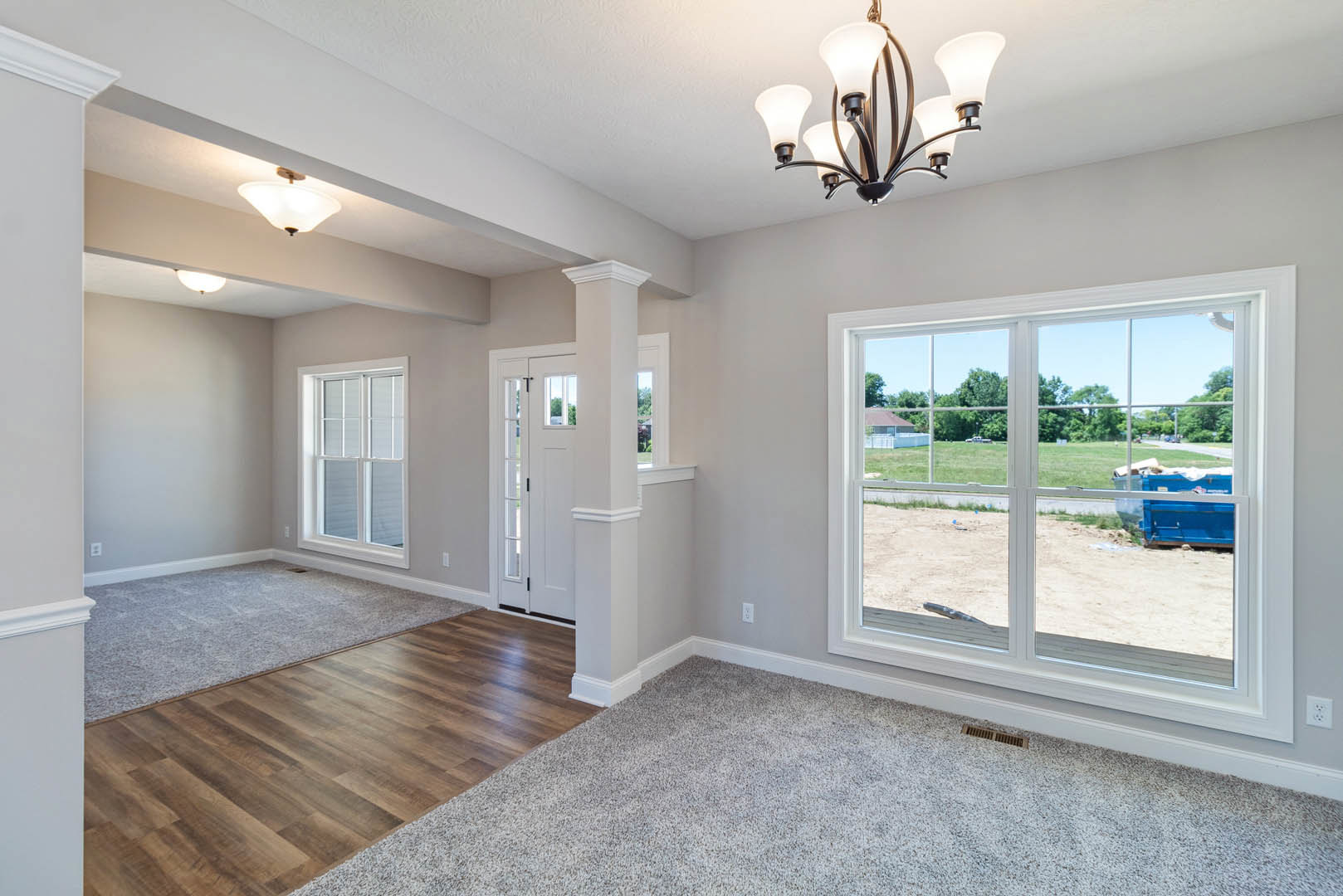 Spacious room featuring a large window overlooking a yard, wood flooring with carpet accent, neutral walls, and a decorative chandelier hanging from the ceiling
