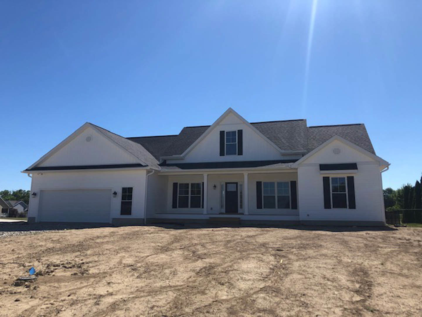 Two-story house with light siding, black front door featuring a square window, white-framed windows, covered porch, and dirt yard under a clear blue sky