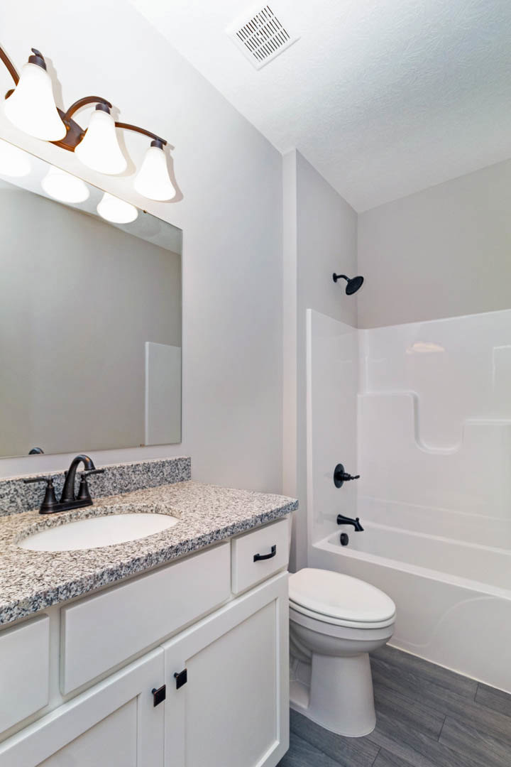 Modern bathroom featuring a white porcelain sink with chrome faucet, matching toilet, glass-enclosed shower with tiled walls, and a sleek light fixture above the vanity.